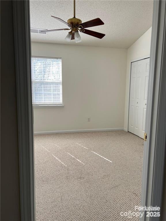 interior space featuring baseboards, carpet flooring, a closet, a textured ceiling, and a ceiling fan