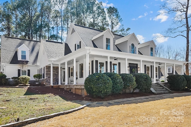 view of front of property with a ceiling fan, roof with shingles, a porch, a front lawn, and stone siding