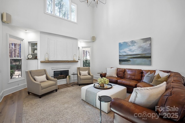 living room featuring baseboards, built in features, a towering ceiling, wood finished floors, and a glass covered fireplace