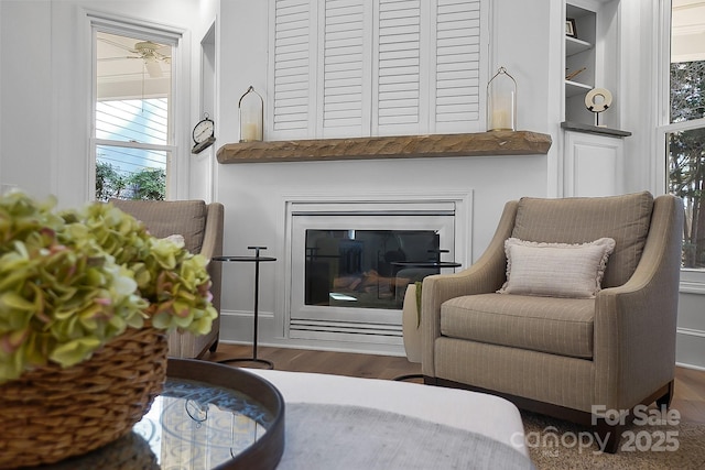 living area with a glass covered fireplace, built in shelves, and wood finished floors