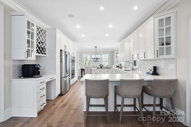 kitchen with a sink, backsplash, wood finished floors, freestanding refrigerator, and a peninsula