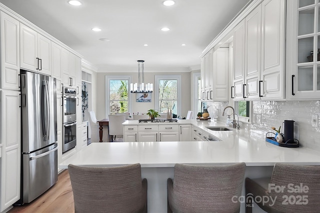 kitchen featuring backsplash, appliances with stainless steel finishes, a peninsula, white cabinetry, and a sink