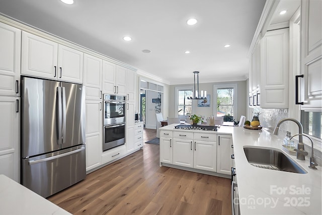 kitchen with a sink, wood finished floors, appliances with stainless steel finishes, white cabinets, and crown molding