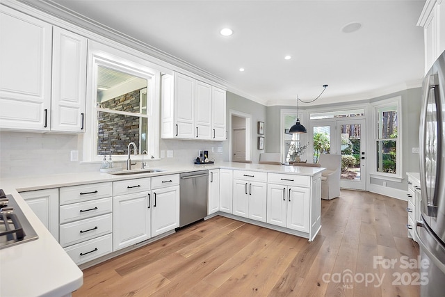 kitchen featuring a peninsula, ornamental molding, a sink, appliances with stainless steel finishes, and white cabinetry