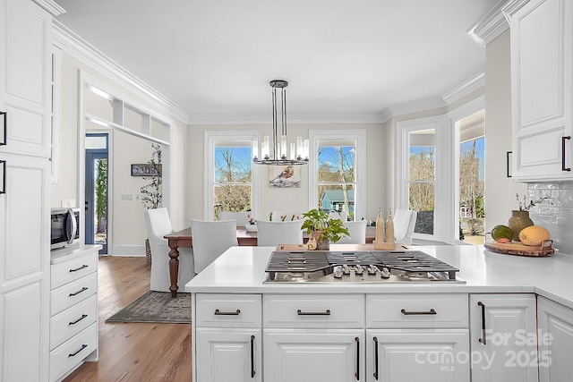 kitchen with appliances with stainless steel finishes, wood finished floors, crown molding, and light countertops