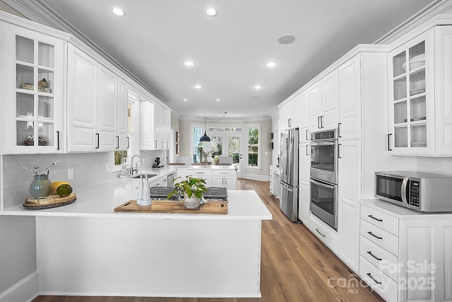 kitchen featuring glass insert cabinets, light countertops, a peninsula, white cabinets, and stainless steel appliances