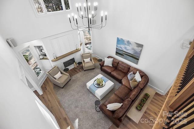 living area featuring a fireplace with flush hearth, a notable chandelier, wood finished floors, a high ceiling, and baseboards