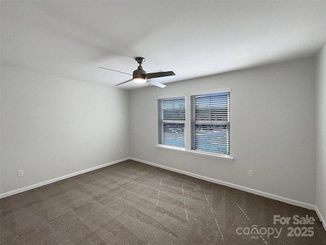 empty room with baseboards, dark carpet, and a ceiling fan