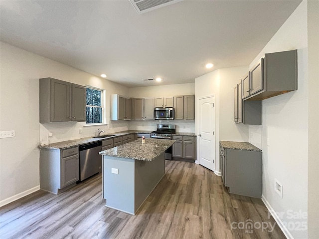 kitchen with visible vents, a kitchen island, appliances with stainless steel finishes, dark wood-type flooring, and a sink