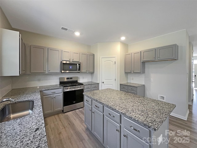 kitchen with light stone counters, a center island, gray cabinets, appliances with stainless steel finishes, and a sink