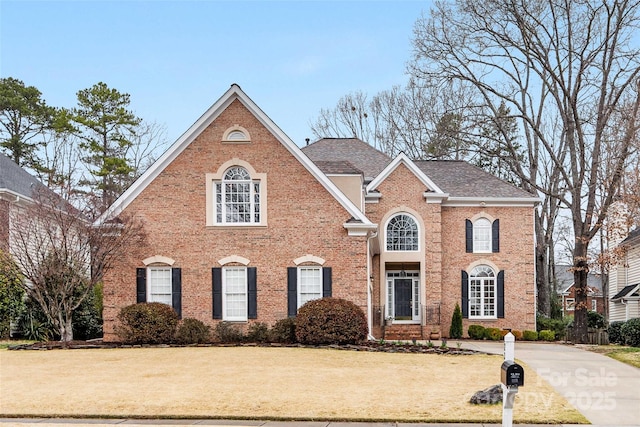 view of front of property with brick siding, a shingled roof, and a front lawn