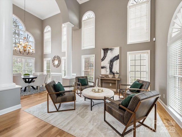 living area with light wood-style floors, decorative columns, a notable chandelier, and a high ceiling