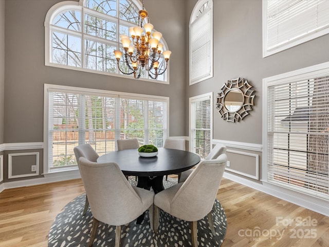 dining space featuring light wood-type flooring, a towering ceiling, and wainscoting