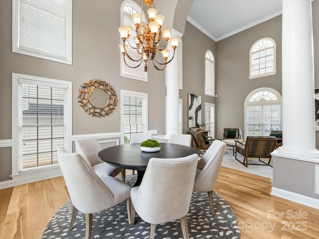 dining area featuring crown molding, light wood-type flooring, a towering ceiling, a notable chandelier, and ornate columns