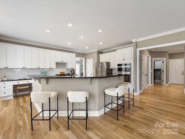 kitchen featuring light wood-style flooring, a kitchen breakfast bar, dark countertops, stainless steel appliances, and white cabinets