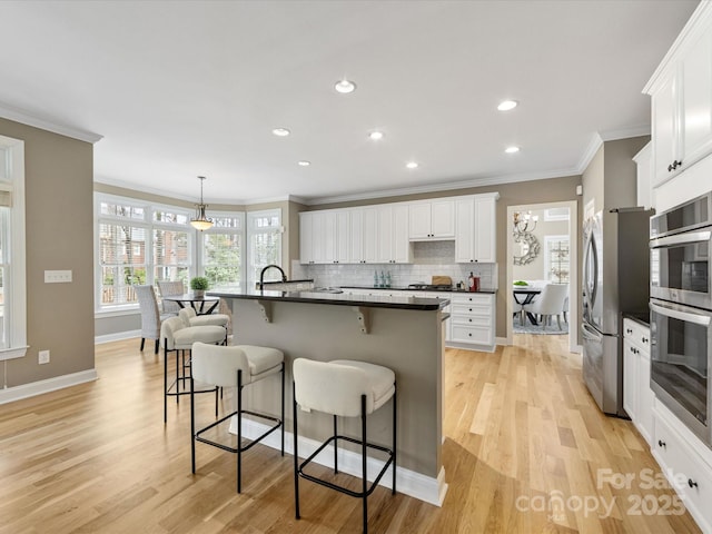 kitchen with dark countertops, light wood finished floors, backsplash, a breakfast bar, and appliances with stainless steel finishes