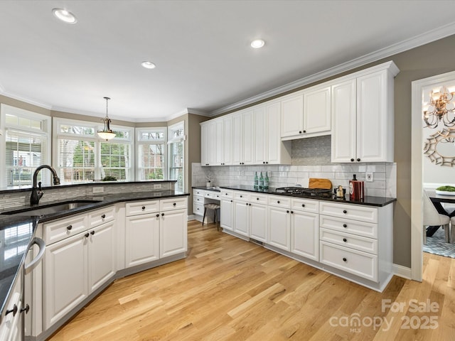 kitchen with light wood finished floors, a sink, white cabinets, crown molding, and backsplash