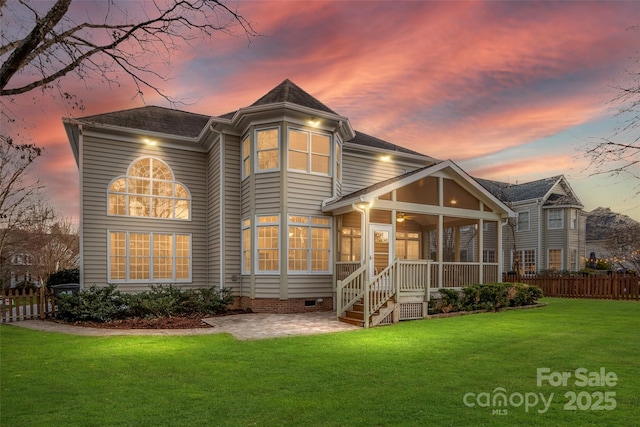 back of property at dusk with crawl space, fence, a yard, and a sunroom