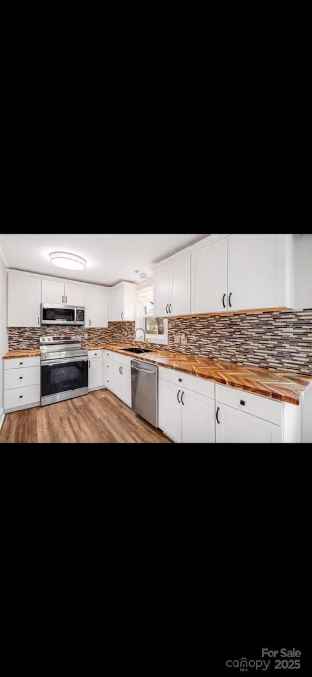 kitchen with light wood-style flooring, stainless steel appliances, butcher block counters, white cabinetry, and decorative backsplash