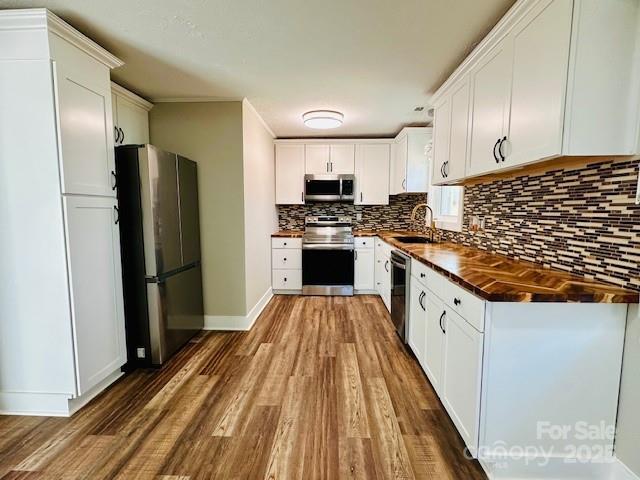 kitchen with a sink, tasteful backsplash, wood finished floors, stainless steel appliances, and white cabinets