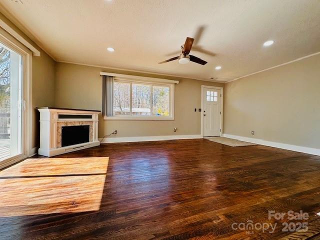 unfurnished living room featuring a fireplace, crown molding, baseboards, and wood finished floors