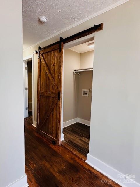 interior space featuring ornamental molding, a textured ceiling, wood finished floors, a barn door, and baseboards