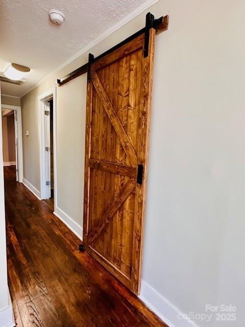 hall featuring a barn door, baseboards, a textured ceiling, and wood finished floors