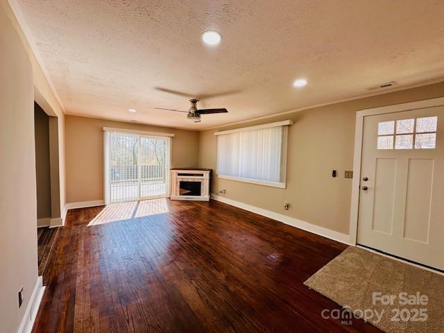 unfurnished living room with visible vents, baseboards, a fireplace, wood finished floors, and a textured ceiling