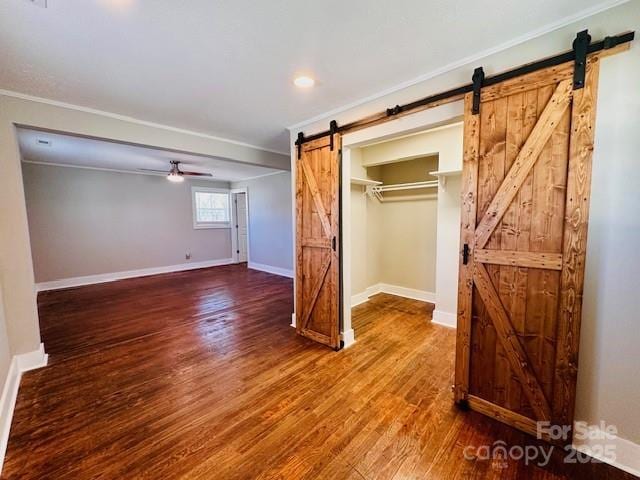 unfurnished bedroom featuring wood finished floors, baseboards, crown molding, a closet, and a barn door