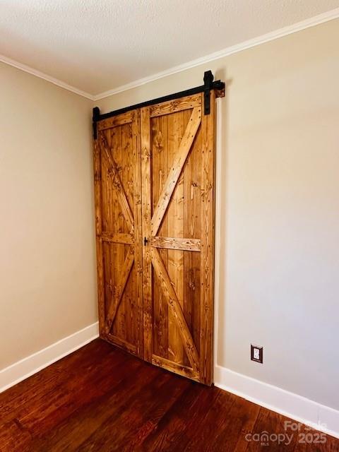unfurnished room featuring a barn door, baseboards, dark wood-style floors, and ornamental molding