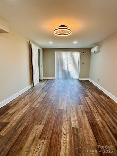 unfurnished living room featuring dark wood-style floors, a wall mounted AC, and baseboards