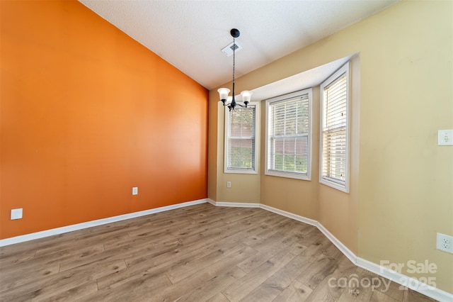 spare room with a notable chandelier, wood finished floors, visible vents, baseboards, and vaulted ceiling