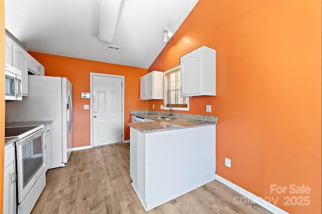 kitchen with white appliances, a sink, visible vents, white cabinets, and vaulted ceiling