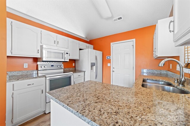 kitchen with visible vents, white cabinets, a sink, white appliances, and a peninsula