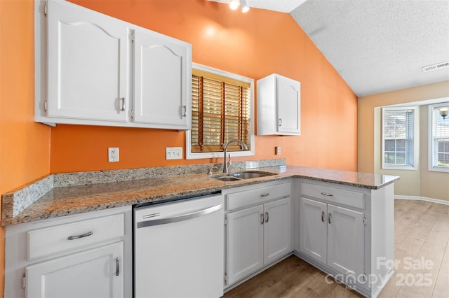 kitchen with visible vents, lofted ceiling, dishwashing machine, a peninsula, and a sink