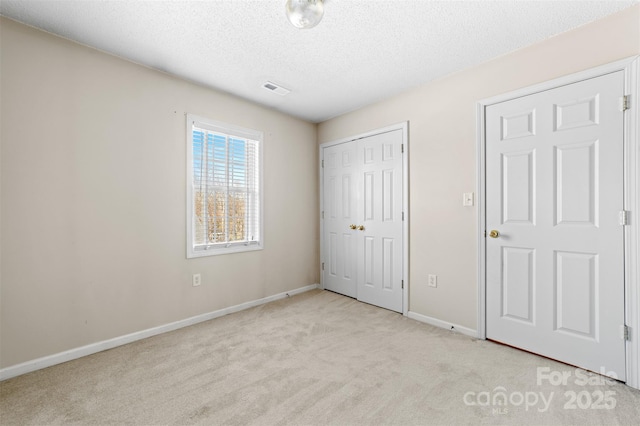 unfurnished bedroom with a textured ceiling, carpet floors, visible vents, baseboards, and a closet