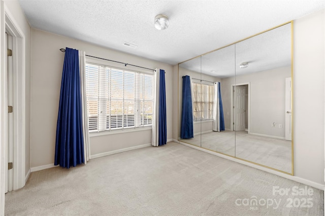 unfurnished bedroom with carpet floors, visible vents, a textured ceiling, and baseboards