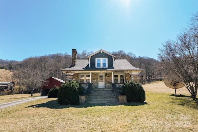 view of front of home with stone siding, a chimney, and a front yard