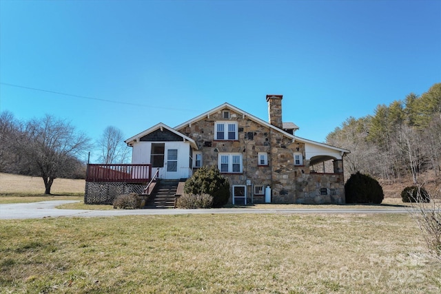 view of front of house with a chimney, stairway, a front yard, stone siding, and a wooden deck