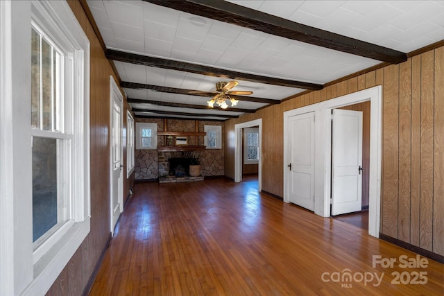 unfurnished living room with a fireplace, wood-type flooring, wood walls, ceiling fan, and beamed ceiling