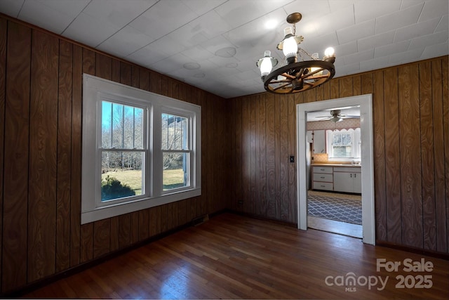 spare room with a sink, wood walls, a chandelier, and dark wood-type flooring