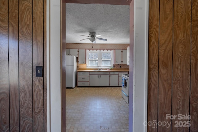 kitchen with white appliances, wallpapered walls, a textured ceiling, light floors, and a sink