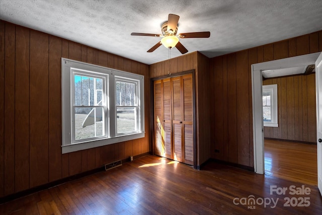 unfurnished bedroom featuring a textured ceiling, visible vents, baseboards, a closet, and hardwood / wood-style floors