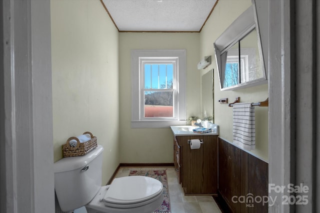 bathroom with baseboards, toilet, vanity, crown molding, and a textured ceiling