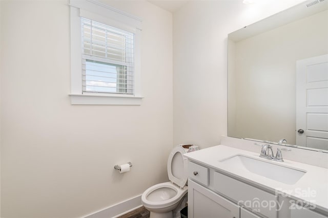 half bathroom with visible vents, toilet, vanity, and baseboards