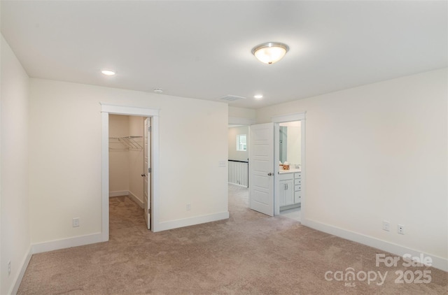 unfurnished bedroom with light colored carpet, visible vents, baseboards, a closet, and a walk in closet