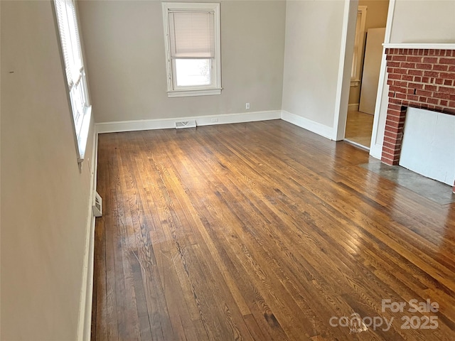 unfurnished living room with dark wood-style floors, a brick fireplace, visible vents, and baseboards