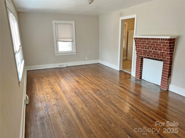 unfurnished living room featuring baseboards, a fireplace, visible vents, and dark wood finished floors