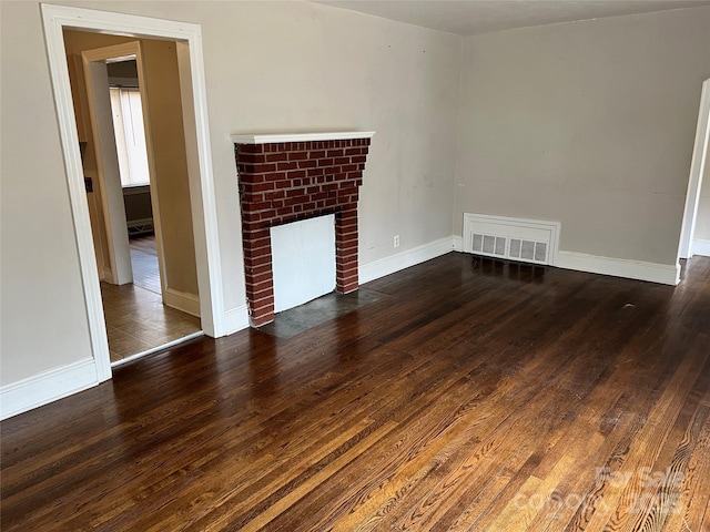 unfurnished living room featuring hardwood / wood-style flooring, a brick fireplace, visible vents, and baseboards