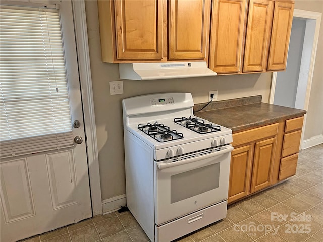 kitchen featuring light tile patterned flooring, under cabinet range hood, baseboards, white range with gas cooktop, and dark countertops